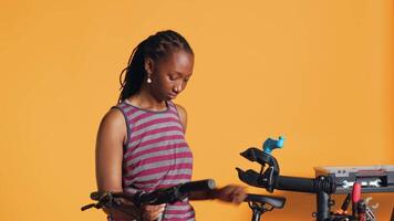 BIPOC mechanic setting up bike repair stand, using it to adjust handlebar and fix broken wheels, studio background. Professional placing bicycle on workstand in tight grip to inspect it, camera A video