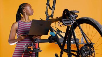 Techniker mit Laptop im Hand Analysieren gebrochen Fahrrad Über Studio Hintergrund warten Reparatur. Spezialist mit Notizbuch zu aussehen zum Ersatz Teile zum Fahrrad auf Reparatur Stand, Kamera b video