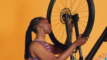 Woman doing bike servicing in studio background atelier shop, searching substitute for defective wheel. Technician fixing faulty bicycle tires and servicing damaged rear derailleur video