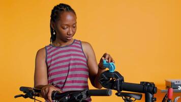 afrikanisch amerikanisch Frau Rahmen oben Fahrrad Reparatur Stand, mit es zu einstellen Umwerfer, Festsetzung gebrochen Räder, Studio Hintergrund. Fachmann Platzierung Fahrrad auf Arbeitsständer zu tun Untersuchung auf Es, Kamera b video