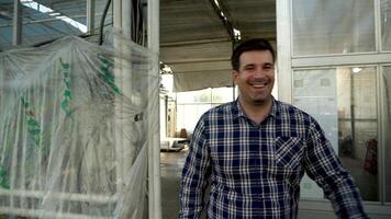 Young smiling farmer walking in greenhouse with growing green salad and modern agriculture technology. video