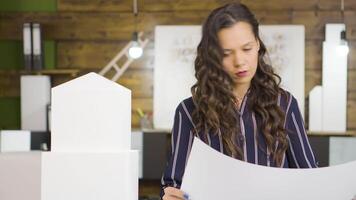 Caucasian female architect in front of building models checking blueprints. video