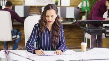 Young female architect taking a sip of coffee while working on blueprints for a new office building, Team of architects. video