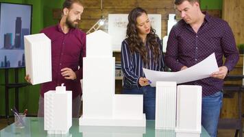 equipo de construcción ingenieros hablando detalles con hembra arquitecto con edificio modelos en frente de el ellos en el mesa. video