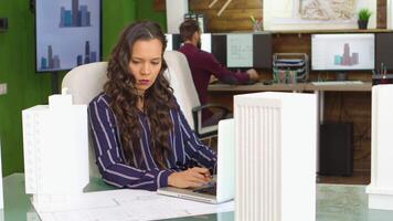 Young female architect working on building project in the office with model of the building. video