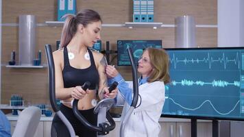 hembra científico adjuntando electrodos en mujer atleta cuerpo. deporte Ciencias en laboratorio. video