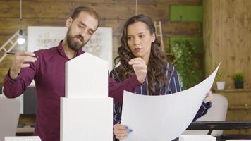 Young architects consulting each other on details for building models and holding blueprints. video