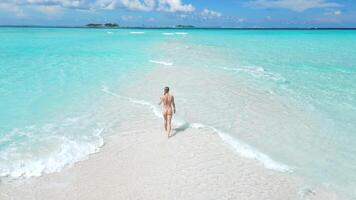 mujer en traje de baño caminando en tropical blanco arena playa con turquesa océano. aéreo ver con hembra en Maldivas video