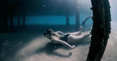 Woman freediver swimming underwater in blue sea. Female swims with fins under the pier video