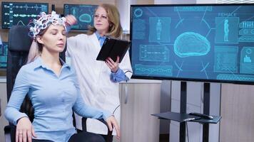 Female scientis in brain activity using her tablet to make adjustmest on her patient headset with sensors for brain activity. video