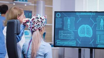 femmina paziente guardare a sua cervello attività su tv schermo indossare un' cuffia per leggere sua cervello dati. video
