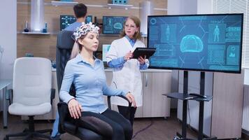 Female patient sitting on a chair with brainwaves sensors in a neuroscience facility for research. Doctor checking patient brain data. video