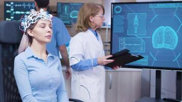 Female doctor looking at tv screen with brain activty while patient wearing brainwave headset in neuroscience clinic. video