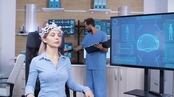 Female patient falling asleep while wearing brain activity scanner. Neuroscientist doctor with her assitant in the background. Brain clinic. video