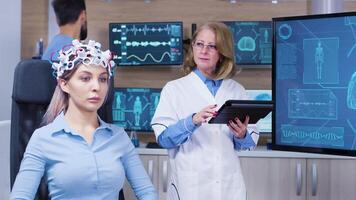 Female patient with eyes closed wearing headset with brain sensors on head. Brain scientist checking female patient. video