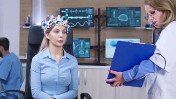 neurologie médecin en portant presse-papiers dans de face de femelle patient cerveau balayage casque. patient en train de lire cerveau données. video