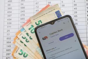 TERNOPIL, UKRAINE - AUGUST 3, 2023 Capitec application on screen on modern smartphone and many bills of euro currency photo