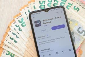 TERNOPIL, UKRAINE - AUGUST 3, 2023 BBVA Spain application on screen on modern smartphone and many bills of euro currency photo