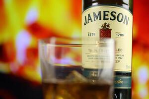 KYIV, UKRAINE - MAY 4, 2022 Jameson original alcohol bottle on wooden table with red fireplace photo