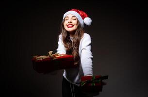 un hermosa niña en un Papa Noel sombrero participación un nuevo años presente. un mujer en un Papa Noel sombrero participación un presente foto