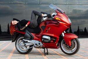 mujer descansando en rojo motocicleta. un mujer cómodamente acostado en parte superior de un vibrante rojo motocicleta. foto
