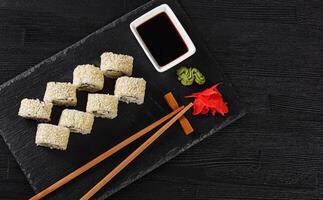 Sushi with salmon on a white plate with wasabi, ginger, soy, chopsticks on a black background photo