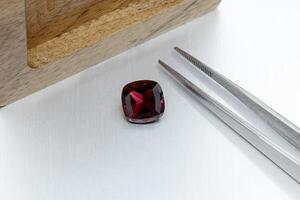 macro mineral faceted stone Garnet with tweezers on a gray background photo