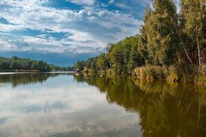 Beautiful view of the lake with blue sky, clouds, and green trees photo