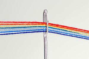 multi-colored threads for sewing in the form of a rainbow pass through an antique needle on a white background photo