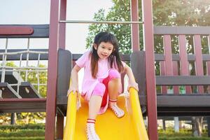 linda asiático niña jugando en el diapositiva en el patio de recreo foto