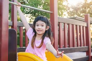 Cute asian girl playing on the slide in the playground photo