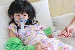 Sick little asian girl inhalation with nebulizer for respiratory treatment photo