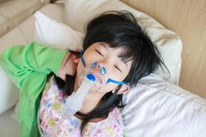 Sick little asian girl inhalation with nebulizer for respiratory treatment photo