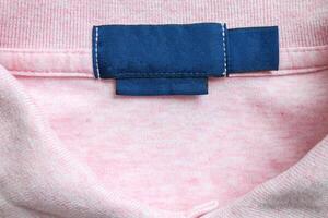 Blank blue laundry care clothes label on pink shirt fabric texture background photo