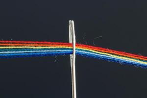 multi-colored threads for sewing in the form of a rainbow pass through an antique needle on a black background photo