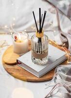 Home fragrance in glass bottle and bamboo sticks with scented candle,  paper book. photo