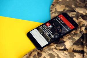 KYIV, UKRAINE - 4 MAY, 2023 TSN ukrainian news portal on smartphone screen with ukrainian flag and camouflage fabric photo