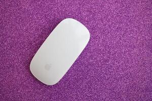KYIV, UKRAINE - NOVEMBER 27, 2023 Apple Magic Mouse 3rd generation lies on sparkling glitter surface photo