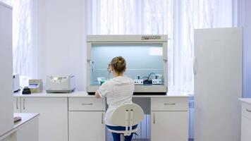 jovem fêmea nutricionista teste Comida amostras dentro laboratório. fêmea investigador trabalhando em uma computador dentro uma laboratório. profissional fêmea cientista é examinando médico amostras costas Visão video