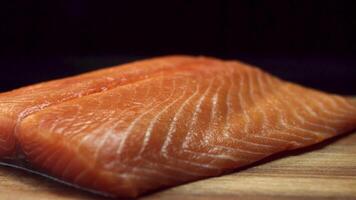 un pedazo de fresco, crudo, rojo pescado en un de madera marrón corte junta, aislado en negro antecedentes. hermosa salmón filete acostado en de madera el cortar junta, Cocinando y sano dieta concepto video