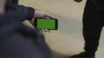 Close up of young male hands holding modern smartphone with green touch screen. Man's hand shows mobile smartphone with green screen to his friend video