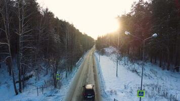 Flying above the car driving through snowy forest at golden winter sunrise. Footage. Aerial view flying from above. Following white car moving on winding road in winter forest with snow trees video