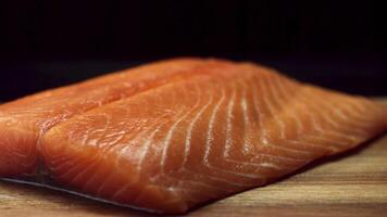 Close up for fresh, yummy salmon steak on wooden cutting board, isolated on black background. Raw red fish fillet on wooden chopping board, cooking, food porn concept. video