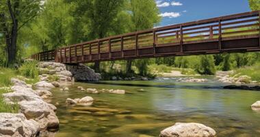 AI generated A Scenic Bridge Over a Sparkling River, Framed by Rocky Banks, Lush Trees, and a Blue Sky with Fluffy Clouds photo