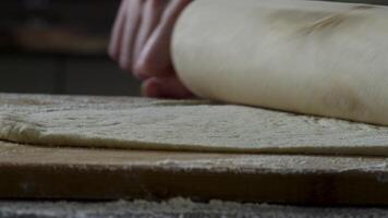 homme roulant en dehors pâte sur cuisine tableau, proche en haut. scène. le cuisinier Rouleaux une pièce de pâte sur le cuisine table avec une roulant broche. proche en haut voir. concept de cuisine et fait maison repas video