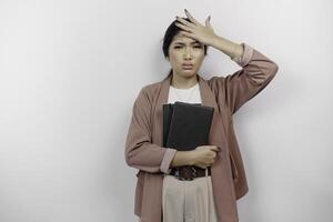 A stressed young Asian student wearing cardigan while holding books, isolated by white background. photo