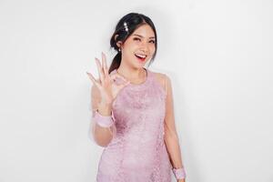 Attractive young Asian woman in pink dress is gesturing OK sign with her fingers, isolated by white background photo