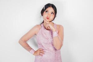 A thoughtful Asian woman wearing pink dress is imagining her thoughts, isolated by white background. photo