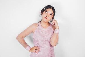 A thoughtful Asian woman wearing pink dress is imagining her thoughts, isolated by white background. photo