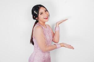 A cheerful Asian woman wearing pink dress is pointing copy space beside her, isolated by white background. photo